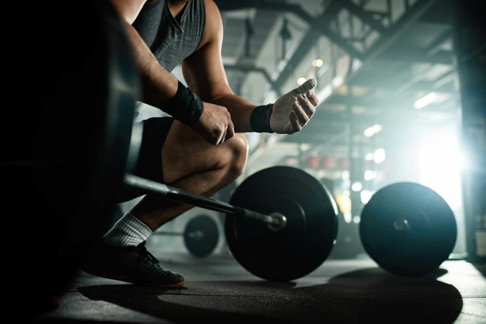 Gros plan d'un sportif avec protège-poignets assis près d'haltères dans la salle de sport fitness à Charmes, ambiance industrielle.